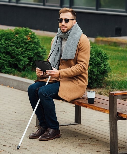 Brailliant BI 20x person sitting with white cane holding Brailliant BI 20x 1