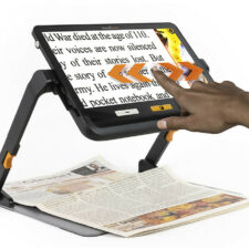 Customer using explorē 12 Portable Magnifier With Stand to read a newspaper