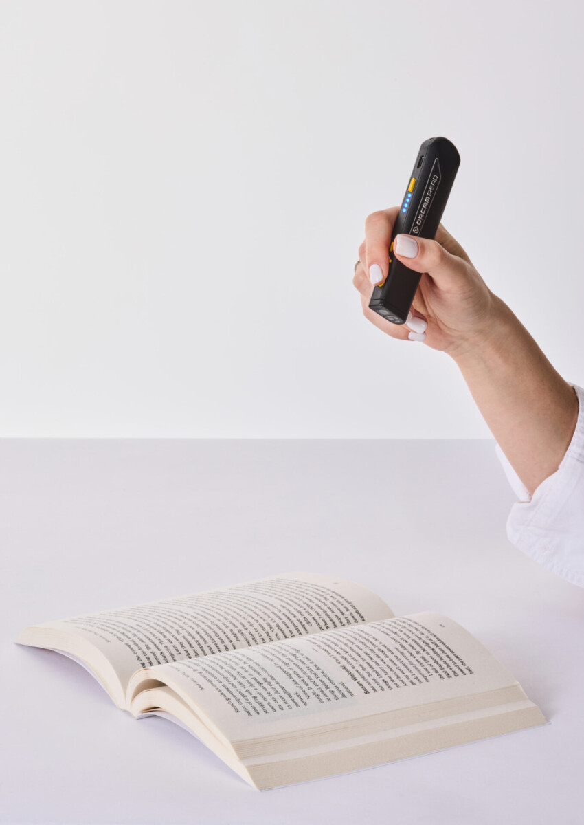 OrCam Read 3 person holding in their right hand pointing to a book