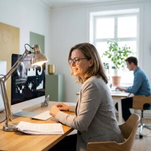 Woman with low vision working at an office desk using an enlarged high-contrast monitor display and a task lamp angled onto her documents